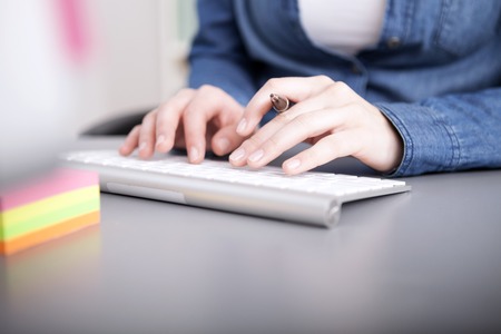 Close up view of the hands of a businesswoman typing in data to her computer on a desktop keyboardの写真素材