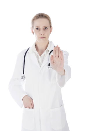 Close up Portrait of a Serious Female Doctor Showing Stop Hand Sign with One Hand in her Pocket and Looking at the Camera. Isolated on White Background.の写真素材