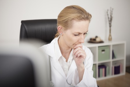 Close up Pensive Blond Female Clinician Thinking So Deep While Looking Down at her Office.の写真素材