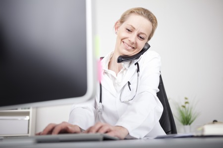 Close up Happy Woman Doctor Calling on the Telephone While Using her Computer on the Tableの写真素材