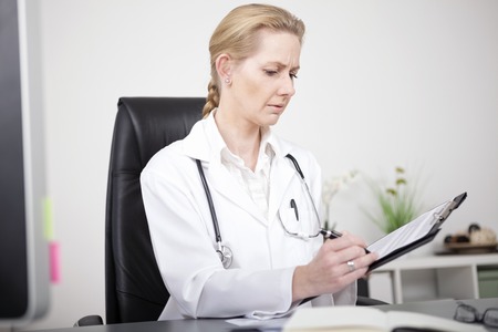 Close up Serious Female Doctor Writing Medical Findings on a Paper While Sitting at her Office.の写真素材