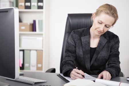 Close up Sitting Businesswoman in Black Business Suit Writing Documents on Top of her Desk Seriously.の写真素材