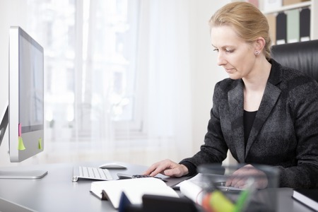 Happy Adult Businesswoman Calculating Something Using a Calculator Device While Sitting at her Worktable.の写真素材