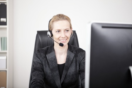 Smiling Female Customer Support in Black Business Attire Sitting at her Office While Facing her Computer Screen.の写真素材