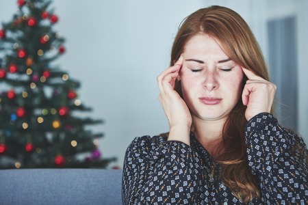 young unhappy girl has headache of christmas stress with tree in backgroundの写真素材