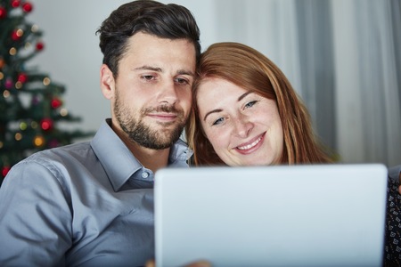 happy young couple use or watch something on tablet pc for christmas on sofa