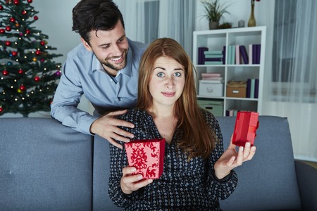 girlfriend looks sceptical to her christmas gift while her boyfriend smile behind herの写真素材
