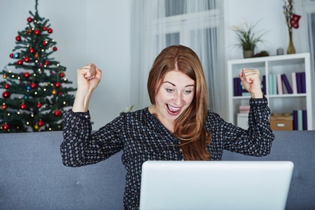 at christmas girl raise arms into the air at laptop as she win something and is very happyの写真素材