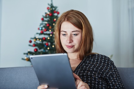 young girl is surfing with laptop at christmas on sofa with christmas tree in backgroundの写真素材