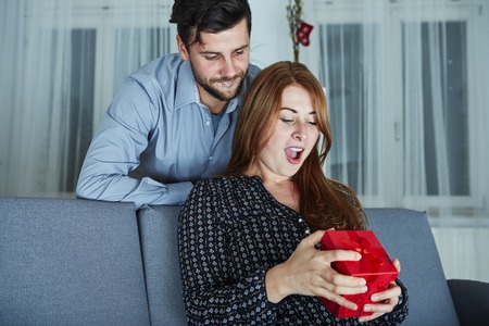 young couple is happy with gift for christmas in front of christmas treeの写真素材