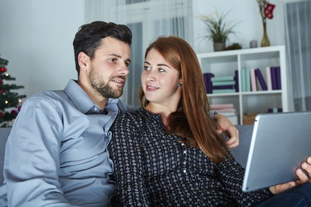 happy young couple use or watch something on tablet pc for christmas on sofaの写真素材