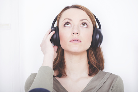 Pensive brown haired girl dressed casual sitting listening to music while looking upwardsの写真素材