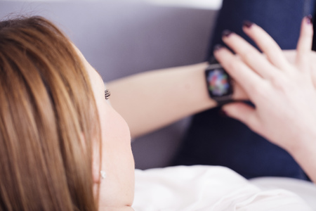Pretty brown haired girl having a rest on sofa taking a look on her smart watchの写真素材