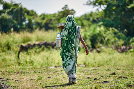 Indian woman in traditional clothes walking in the field with watering can.