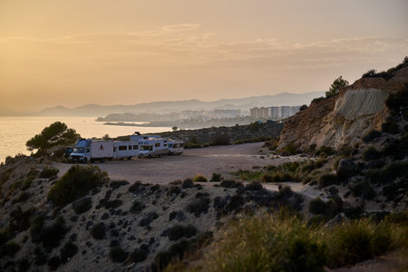 Golden hour coastal landscape cliffs camping vehicles Mediterranean Spain dramatic sunset lighting...