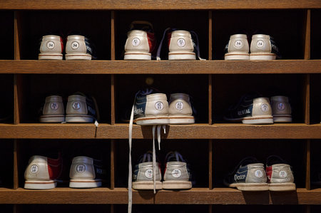 Vintage bowling rental shoes organized in wooden cubby shelves grid pattern indoor ambient lighting...