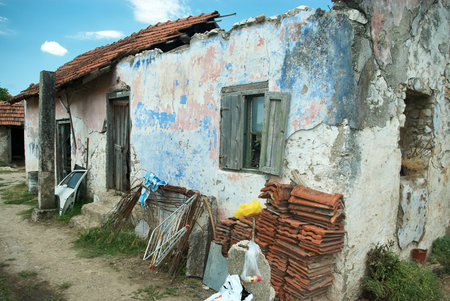 Dilapidated old house with colorful peeling paint walls and red tile roof in rural Serbian village settingのeditorial素材