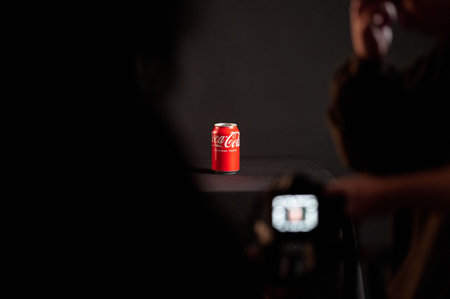 Spotlighted coca-cola can surrounded by smoke on a black table with audience silhouettes, studio...