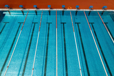 Top-down aerial shot of a blue swimming pool with empty lanes, clean water, and geometric symmetry,...