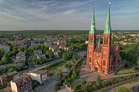Drone photo of the red brick Basilica of St. Anthony in Rybnik, Poland, captured from high altitude with blue sky and city landscape, emphasizing architectural symmetry and vibrant color contrast.の写真素材