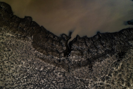 Water puddle edge cracked mud aerial detail view mining area industrial texture pattern brown beige environmental landscape abstract surface sedimentの写真素材
