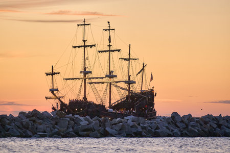 Historic galleon anchored at rocky jetty during sunset, illuminated sails and rigging, maritime heritage, twilightの写真素材