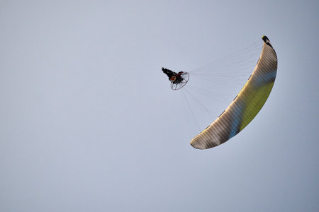 Paraglider flying in clear blue sky above sea, extreme sport action, aerial view, adventure activity...