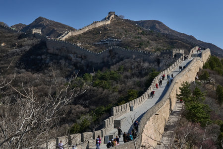 Dramatic Great Wall defensive tower on steep rocky peak with distant fortress, spring landscape, barren trees, panoramic mountain vistaの写真素材