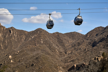 Aerial cable car crossing over steep rocky mountains with sparse vegetation and scenic landscape