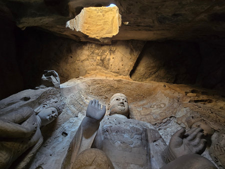 Ancient Buddhist stone Buddha figures in Yungang Grotto cave illuminated by natural light and warm tones, high angle shot, archaeological detailの写真素材