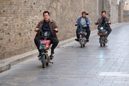 Men on electric scooters in historic brick alley, ancient Chinese architecture, daytime street photography, horizontal orientation, shallow depth of field, natural daylight, documentary composition, lifestyle and transportation themes, stock use for traveのeditorial素材
