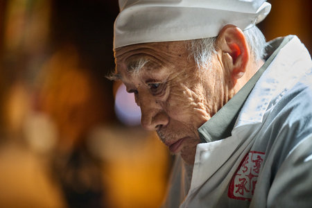 Senior man in white uniform at outdoor counter or stand at night, service worker portrait, evening...