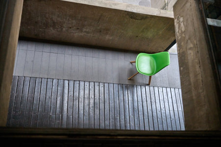 Vertical shaft green modern chair suspended from brutalist ceiling in warehouse gallery spaceのeditorial素材