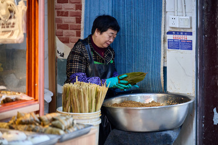 Traditional Chinese street vendor preparing snacks, blue mesh curtain background, authentic urban sceneのeditorial素材