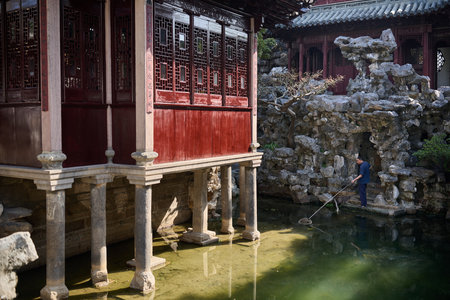 Craftsman raking garden pond with traditional Chinese pavilion, lattice doors and decorative rockery, maintenance workのeditorial素材