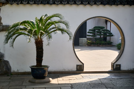 Asian courtyard with circular moon gate, potted palm plant and traditional white walls, peaceful garden designのeditorial素材