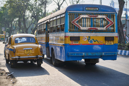 Yellow taxi and blue bus on urban road in India