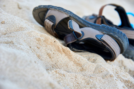 Close up view of a pair of brown leather walking sandals resting on the sand at a beach.