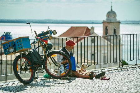 A street performer sitting with his dogs and a loaded bicycle overlooking a church and the Tagus...