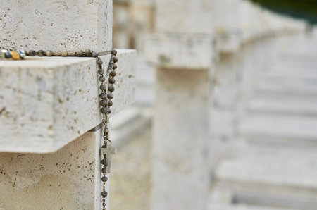 Detail of a rosary on a stone cross with blurred rows of graves in the background, Polish War...