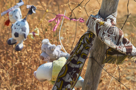 Stuffed animals and a patterned scarf tied to a barbed wire fence at a memorial site in Italy,...