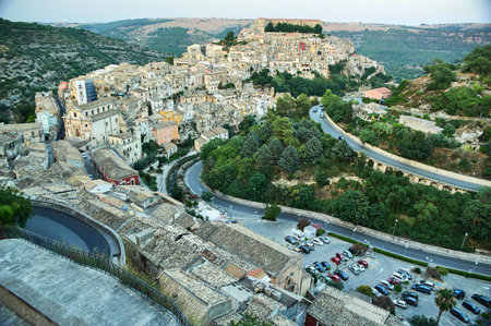 Wide panoramic view of Ragusa Ibla hilltop town with a winding road and parking lot in Sicily, Italy, Europe.のeditorial素材