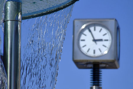 Detailed view of a modern outdoor street clock through the spray of a water fountain, Rybnik,...