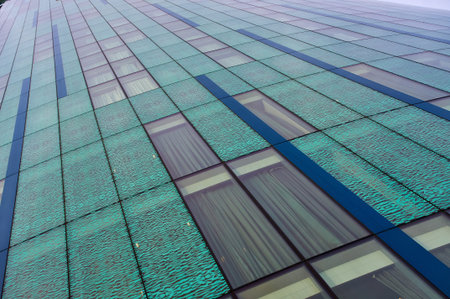Low angle architectural detail of a modern glass skyscraper facade with green and blue panels,...