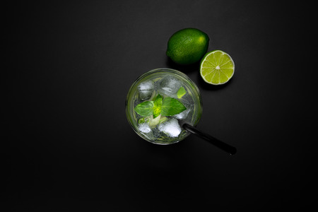 Drink in a glass with limes ice cubes and a black straw, on a black matte background, shot from...