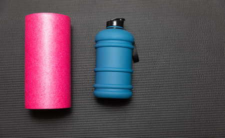 Sports bottle and pink foam roller on a black background. Fitness conceptの写真素材