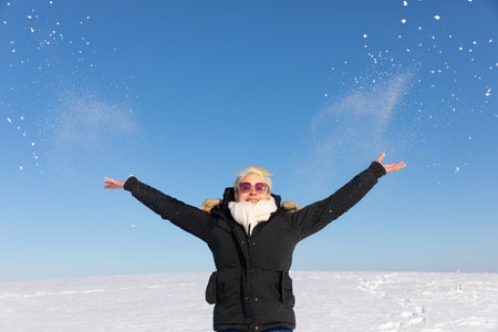 Happy woman throwing snow in the air on a background of blue skyの写真素材