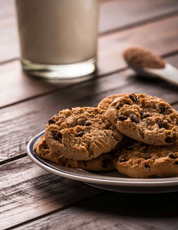 Pile of Delicious Chocolate Chip Cookies on a Plate with Milk glass and a teaspoon of cocoa