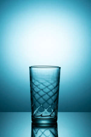 Back lit empty glass on a reflective surface with bluish vignette. copy spaceの写真素材