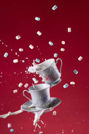 two porcelain cups and saucer flying with splash of milk and marshmallows on a pink backgroundの写真素材